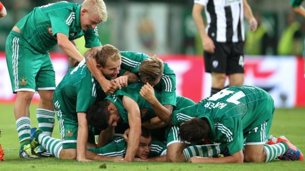 Fußballspieler in grünen Trikots feiern auf dem Rasen ein Tor.