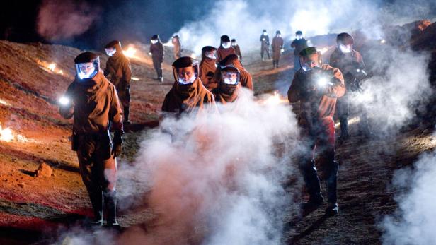 Eine Gruppe von Personen in Schutzanzügen und Helmen steht im Nebel.