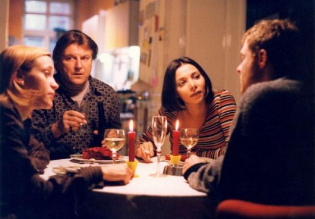 Vier Personen sitzen bei Kerzenlicht und Wein an einem Tisch.