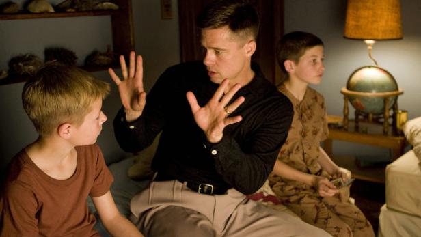 Brad Pitt gestikuliert mit seinen Händen, während er mit zwei Jungen in einem Schlafzimmer sitzt.