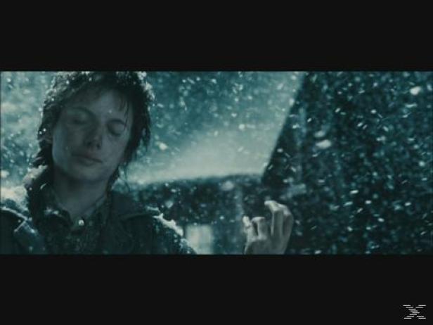 Ein junger Mann steht im Schneefall, das Gesicht dem Himmel zugewandt.