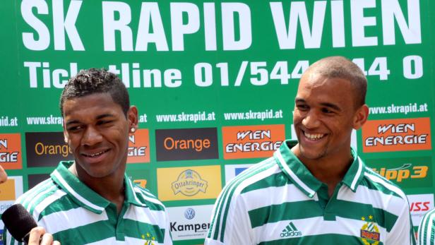 Zwei lächelnde Fußballspieler von Rapid Wien vor einem Werbebanner des Vereins.
