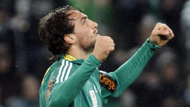 Ein Fußballspieler jubelt mit erhobenen Fäusten auf dem Spielfeld.