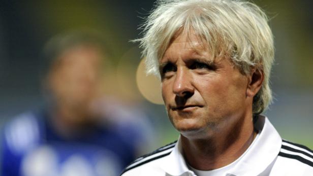 Ein Mann mit blonden Haaren und einem weißen Hemd mit schwarzen Streifen blickt nachdenklich zur Seite.