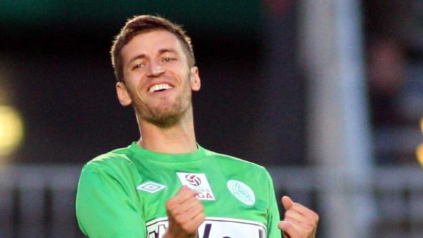 Ein lächelnder Fußballspieler in einem grünen Trikot jubelt.