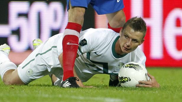 Ein Fußballspieler liegt auf dem Rasen und hält einen Ball.
