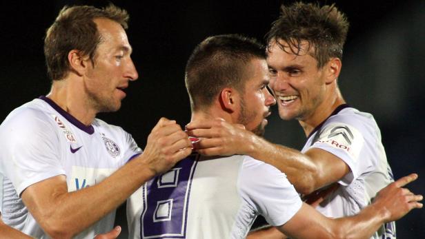 Drei Fußballspieler in weißen Trikots umarmen sich und feiern.