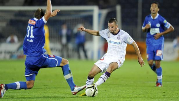 Ein Fußballspieler in Weiß versucht, den Ball an einem Gegenspieler vorbeizuspielen.