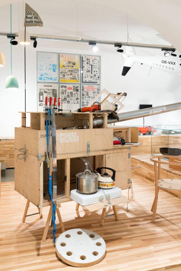 Eine Installation mit Werkzeugen, Kochutensilien und Designplakaten in einem Ausstellungsraum.