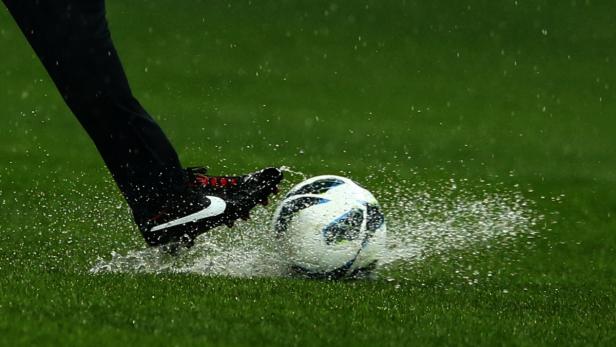 Ein Fußball wird bei Regen von einem Fuß mit Fußballschuh getroffen.