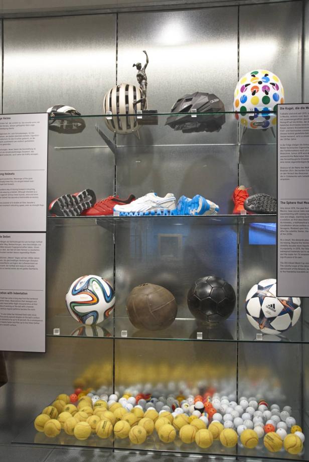 Eine Vitrine mit Helmen, Schuhen, Fußbällen und Tennisbällen.