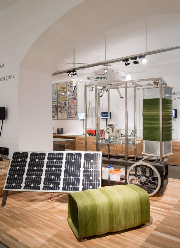 Eine Installation mit Solarmodulen, einem Schiebel-Helikoptermodell und einem grünen Sitzmöbel.