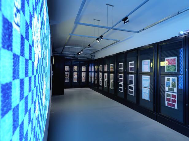 Ein Ausstellungsraum mit Mustern in Vitrinen und einer blau beleuchteten Wand.