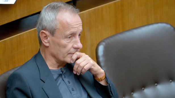 Ein Mann sitzt nachdenklich da, die Hand am Kinn.