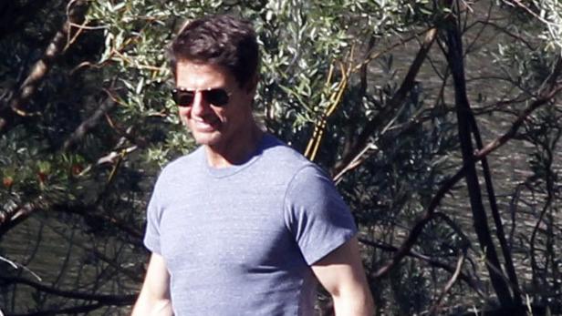 Tom Cruise mit Sonnenbrille und blauem T-Shirt vor Bäumen.