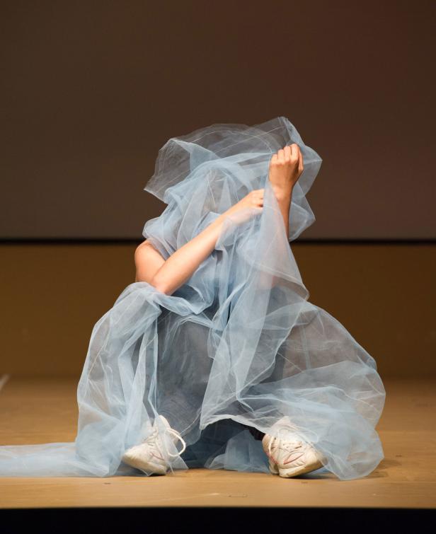 Eine Person sitzt auf dem Boden, gehüllt in einen hellblauen Schleier.