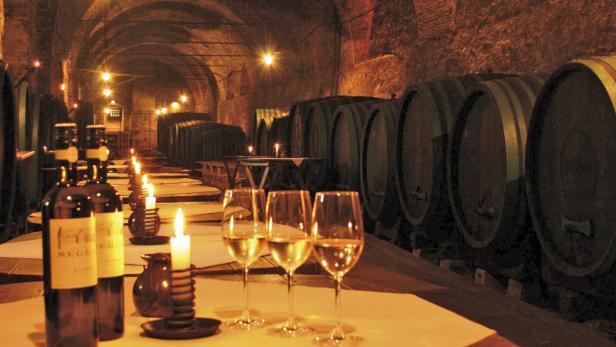 In einem Weinkeller stehen Tische mit Weinflaschen, Gläsern und Kerzen bereit.