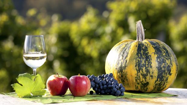 Ein Glas Wein, Äpfel, Trauben und ein Kürbis auf einem Tisch im Freien.