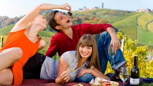 Drei Freunde machen ein Picknick in einem Weinberg und essen Trauben.