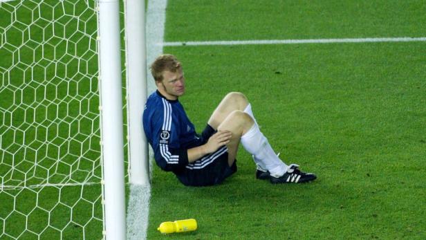 Ein Fußballtorwart sitzt erschöpft am Pfosten.