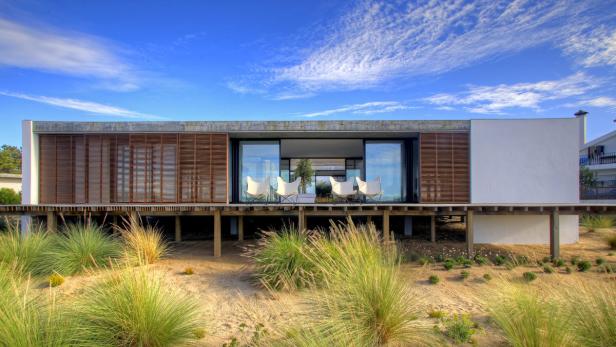 Ein modernes Haus auf Stelzen mit einer Terrasse und Blick auf den Strand.