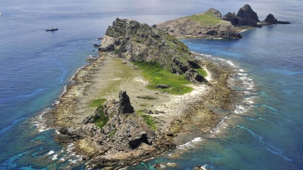 Luftaufnahme einer felsigen Inselgruppe mit einem Schiff im Hintergrund.