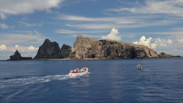 Ein Boot mit Menschen fährt auf dem Meer vor einer felsigen Insel.