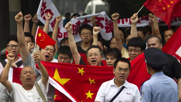 Eine Menschenmenge demonstriert mit erhobenen Fäusten und chinesischen Flaggen.