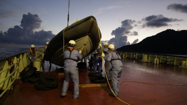 Eine Gruppe von Personen hievt ein Schlauchboot an Deck eines Schiffes.