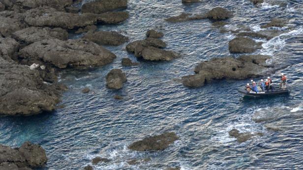 Ein Schlauchboot mit Personen in Schutzkleidung fährt zwischen Felsen hindurch.