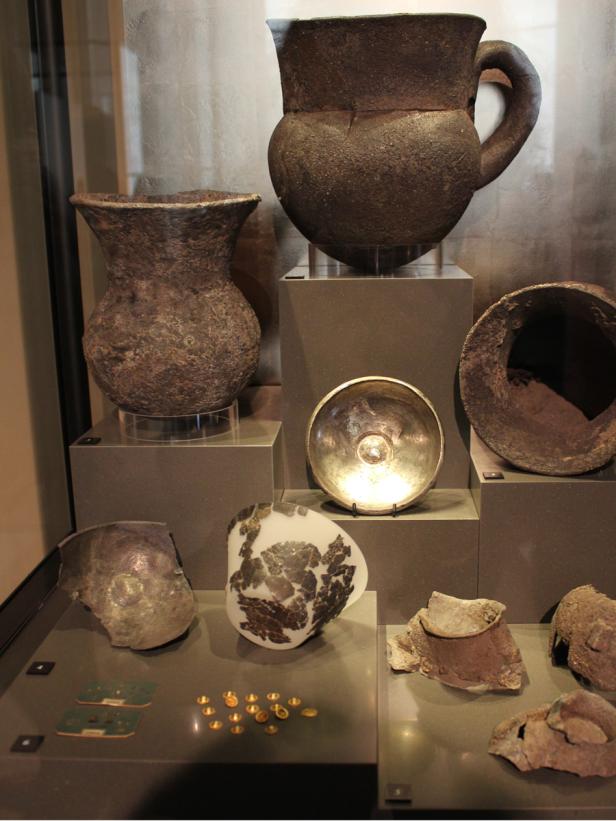 Eine Sammlung antiker Töpferwaren und Artefakte in einer Museumsvitrine.