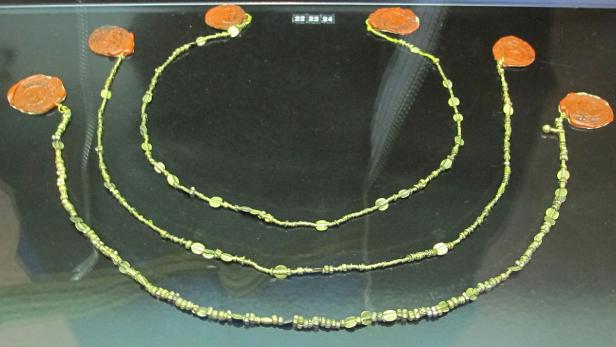 Drei goldene Halsketten mit Siegeln liegen auf einer schwarzen Oberfläche.