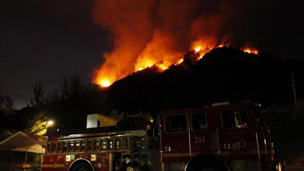 Ein rotes Feuerwehrauto steht vor einem Hügel, der in Flammen steht.