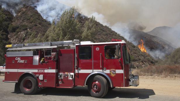 Ein rotes Feuerwehrfahrzeug von Cal Fire steht vor einem Waldbrand.