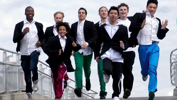 Eine Gruppe junger Männer in Sakkos und Trainingshosen rennt eine Treppe hinunter.