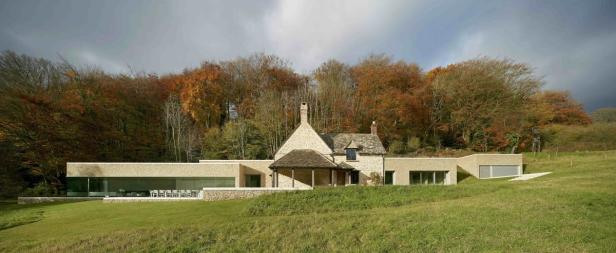 Ein modernes Haus mit traditionellen Elementen vor einem herbstlichen Wald.