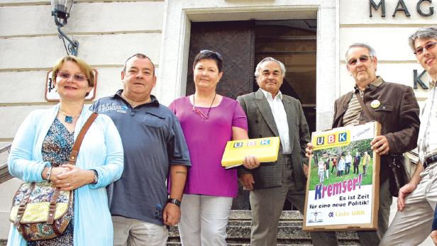 Eine Gruppe von Personen steht vor einem Gebäude und hält Schilder der „Liste UBK“ hoch.