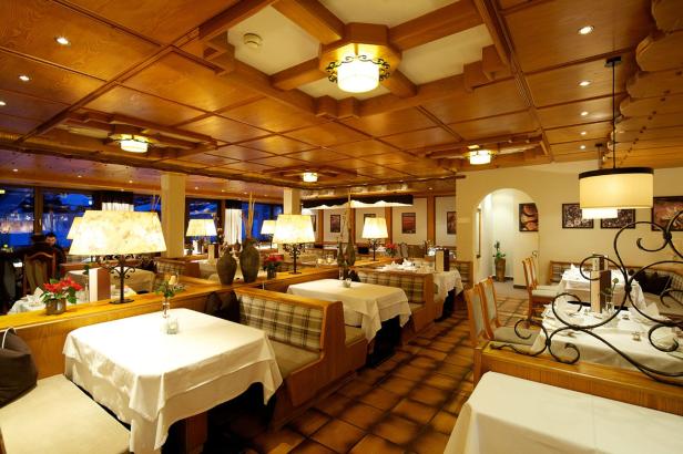 Innenansicht eines eleganten Restaurants mit Holzbalkendecke und gedeckten Tischen.