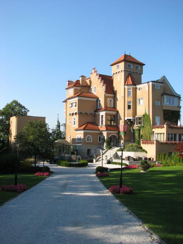 Ein großes, gelbes Schloss mit roten Dächern und einem gepflegten Garten im Vordergrund.