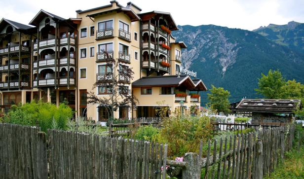 Das Hotel Wiesenhof vor einer Bergkulisse, umgeben von einem Holzzaun und üppiger Vegetation.