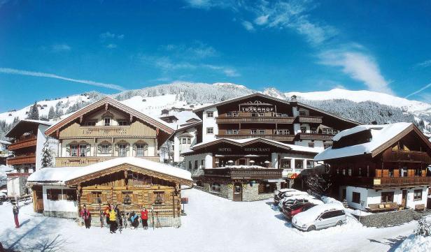 Das Hotel Tuxerhof in einer verschneiten Winterlandschaft mit Skifahrern im Vordergrund.