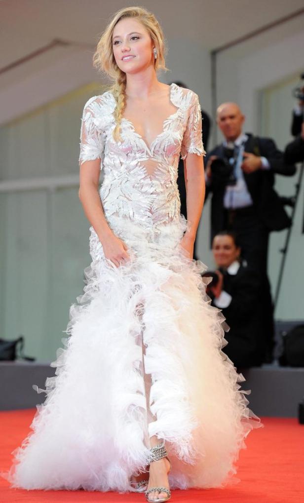 Eine Frau in einem weißen, federartigen Kleid auf einem roten Teppich.