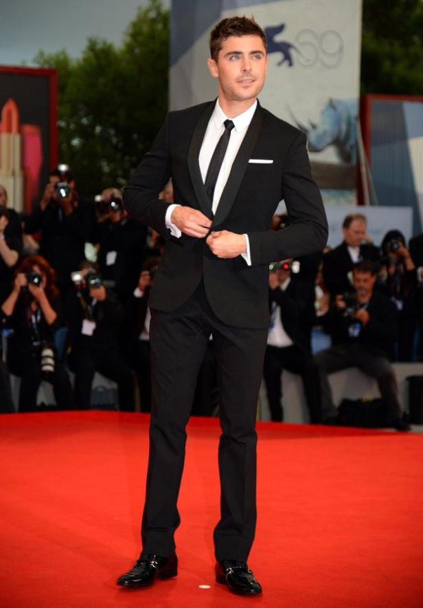 Zac Efron auf einem roten Teppich, in einem schwarzen Anzug.