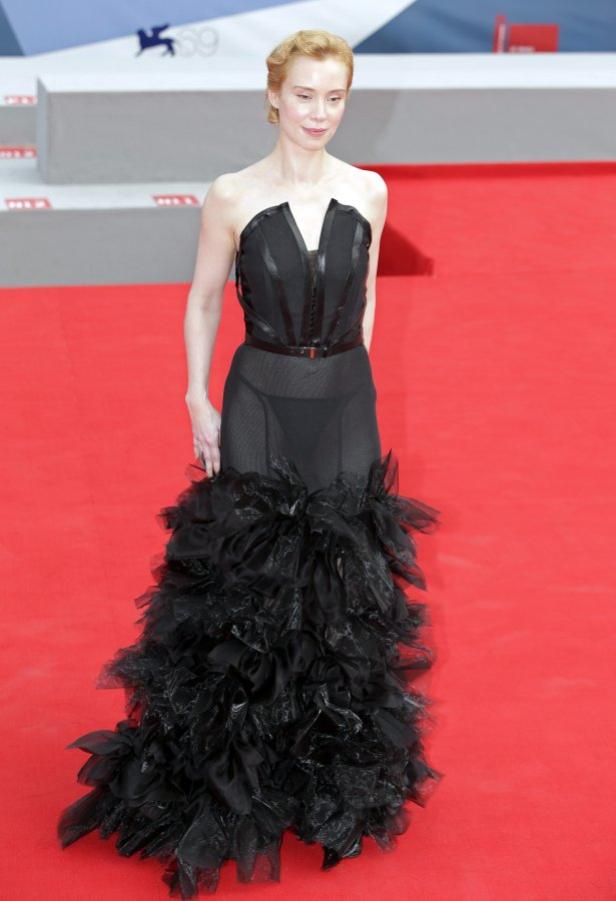 Eine Frau in einem schwarzen, bodenlangen Kleid auf einem roten Teppich.