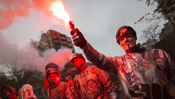 Demonstranten mit roten Fackeln und „Guy Fawkes“-Masken bei einer Kundgebung.