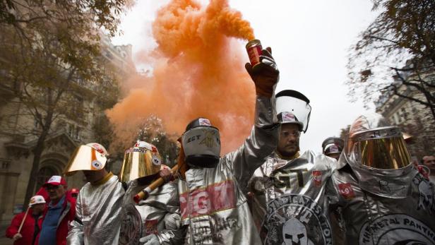 Eine Gruppe von Demonstranten in silbernen Schutzanzügen zündet Rauchbomben.