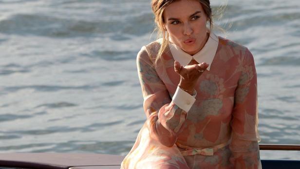 Eine Frau in einem geblümten Kleid schickt einen Kuss vor einem Gewässer.