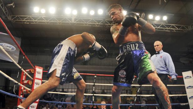 Zwei Boxer kämpfen im Ring, während ein Schiedsrichter zusieht.