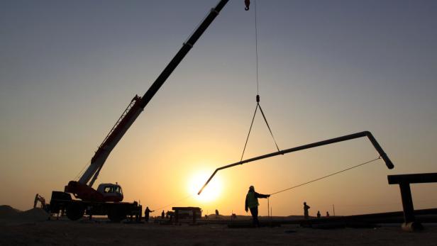 Eine Kran hebt ein Rohr auf einer Baustelle bei Sonnenuntergang.