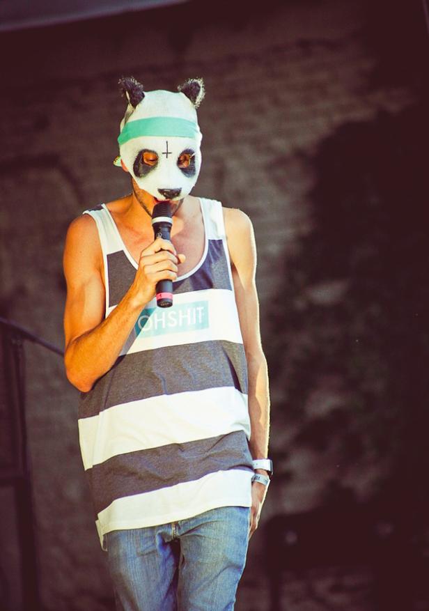Ein Mann mit Panda-Maske und Tanktop spricht in ein Mikrofon.